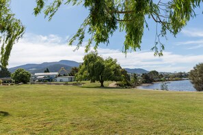 A grassy area with a large tree, a building, and mountains in the background. - Riverfront Motel & Restaurant (Rosetta)