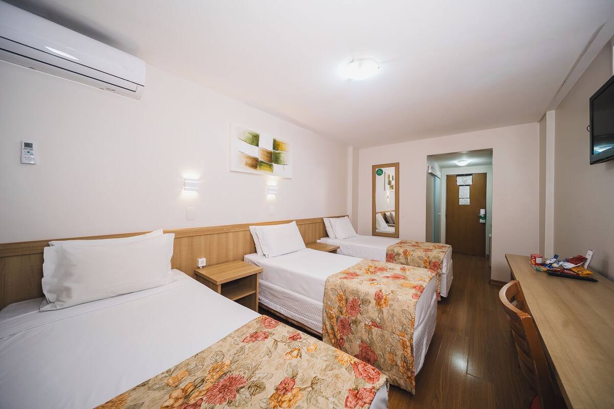 A hotel room with three beds, a wooden headboard, a flat-screen TV, and a small table.