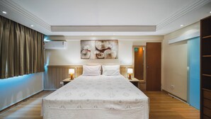 Una camera d'albergo con un letto grande, due comodini con lampade, un condizionatore fissato al muro e un grande quadro astratto sopra il letto.