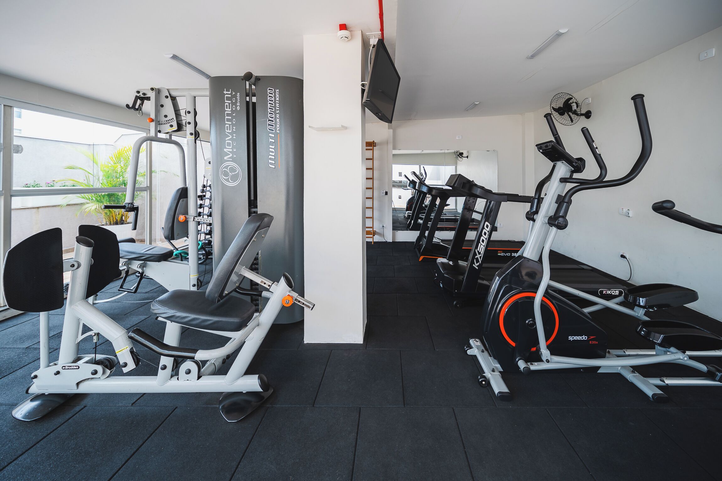 Ein Fitnessstudio mit verschiedenen Trainingsgeräten, darunter Laufband, Kraftgeräte und ein Ergometer.