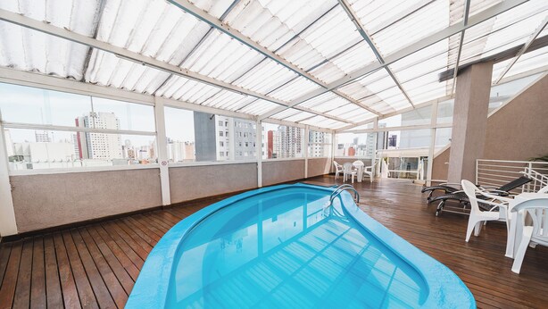 Una piscina sul tetto con un'incorniciatura in vetro, un pontile in legno e vista sulla città.