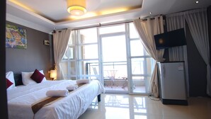A hotel room with a large bed, a flat-screen TV, a refrigerator, and a balcony with a table and chairs. - Pillar Hotel (Phnom Penh)