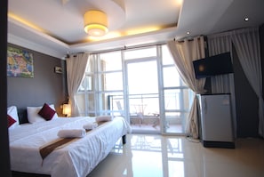 A hotel room with a large bed, a flat-screen TV, a refrigerator, and a balcony with a table and chairs.