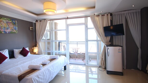 A hotel room with a bed, a TV, a refrigerator, and a balcony with a table and chairs. - Pillar Hotel (Phnom Penh)
