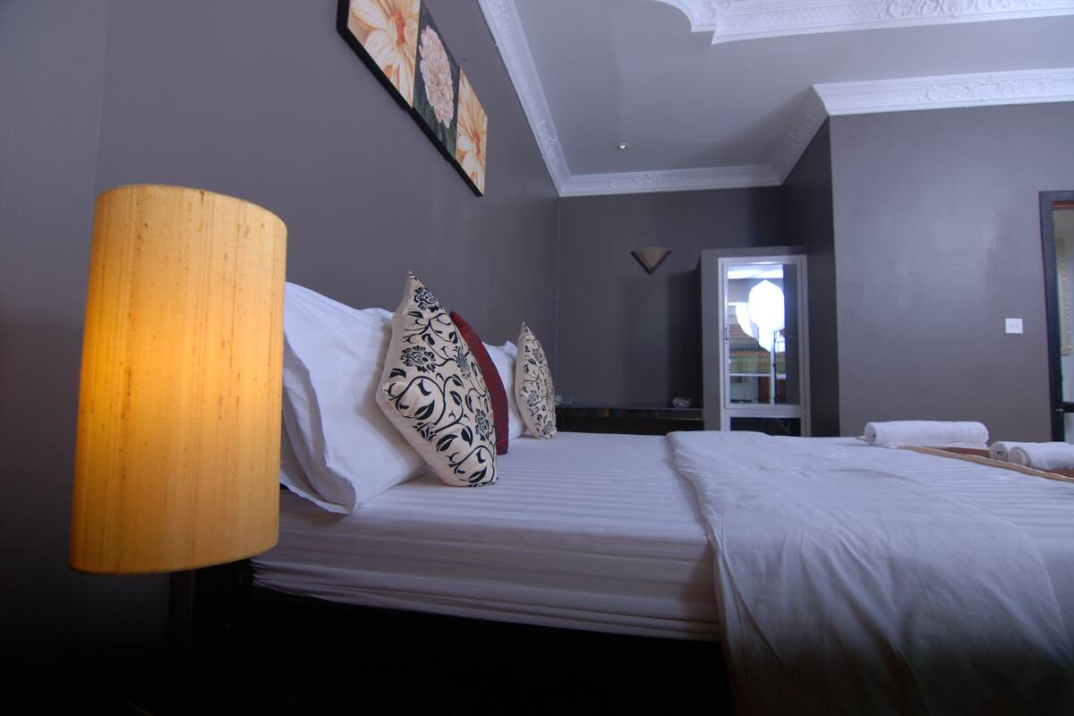 A hotel room with a bed, a large lamp, and a mirror.