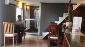 A hotel lobby with a reception desk, two wooden chairs, a staircase, and a potted plant. - Pillar Hotel (Phnom Penh)