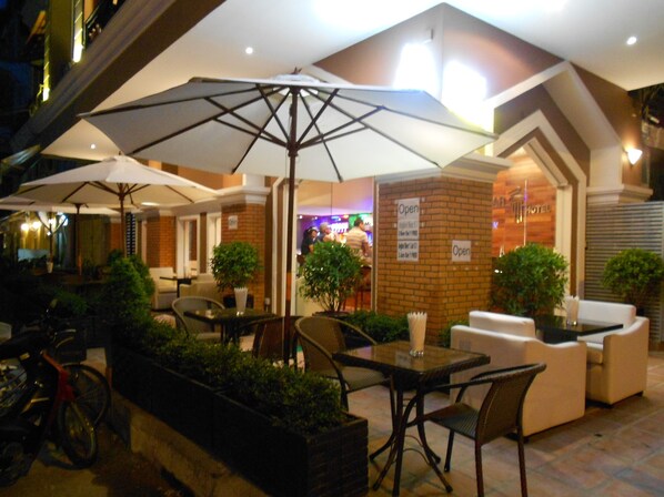 An outdoor seating area with tables and chairs, umbrellas, and potted plants.