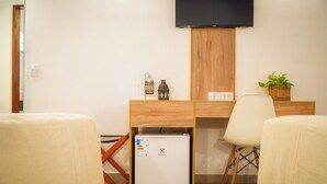 Une chambre d’hôtel avec un bureau en bois, un petit réfrigérateur, un téléviseur fixé au mur et une plante en pot.