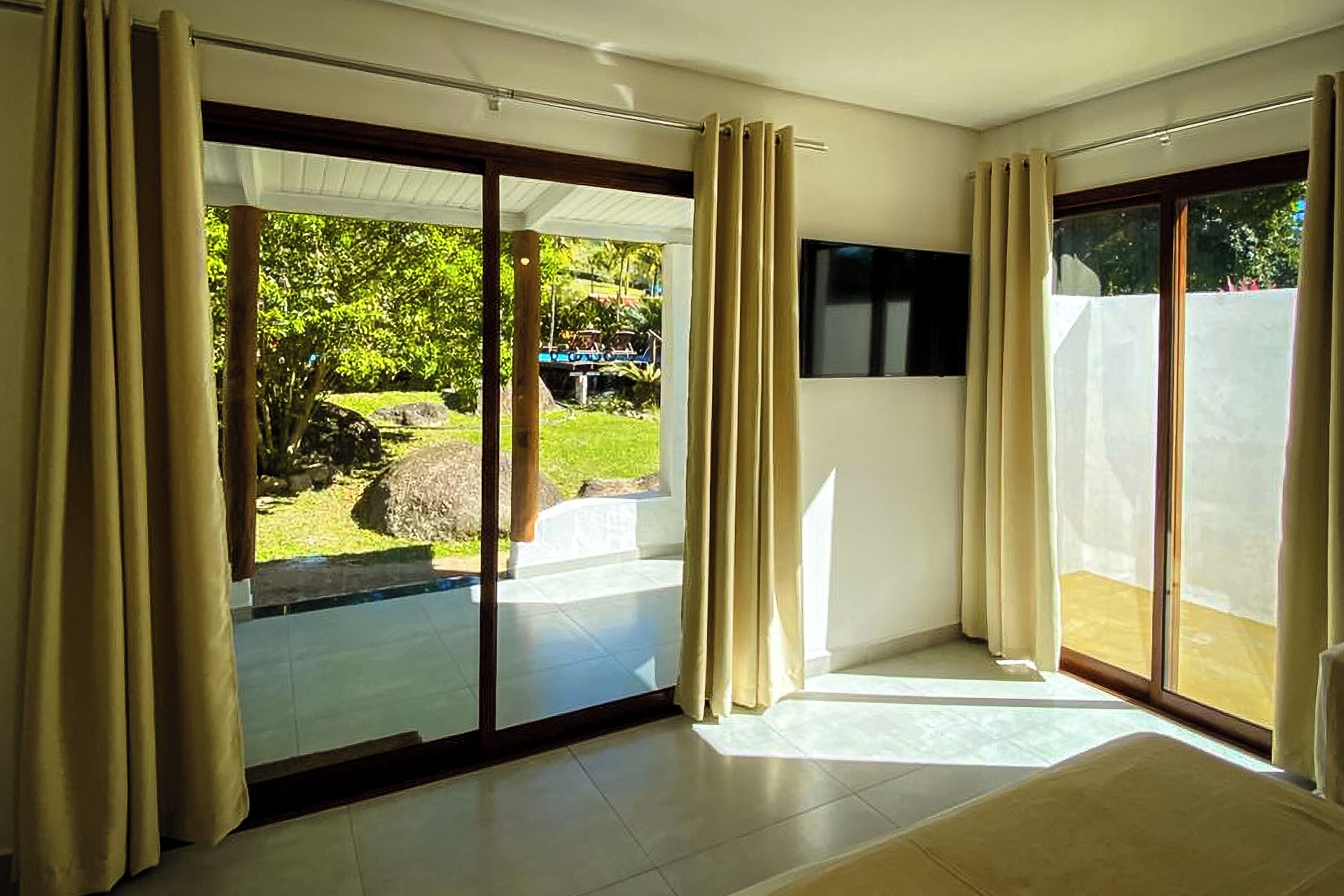 Quarto moderno com grandes portas de vidro deslizantes que dão para um jardim, uma TV de tela plana na parede e um grande janela com cortinas.