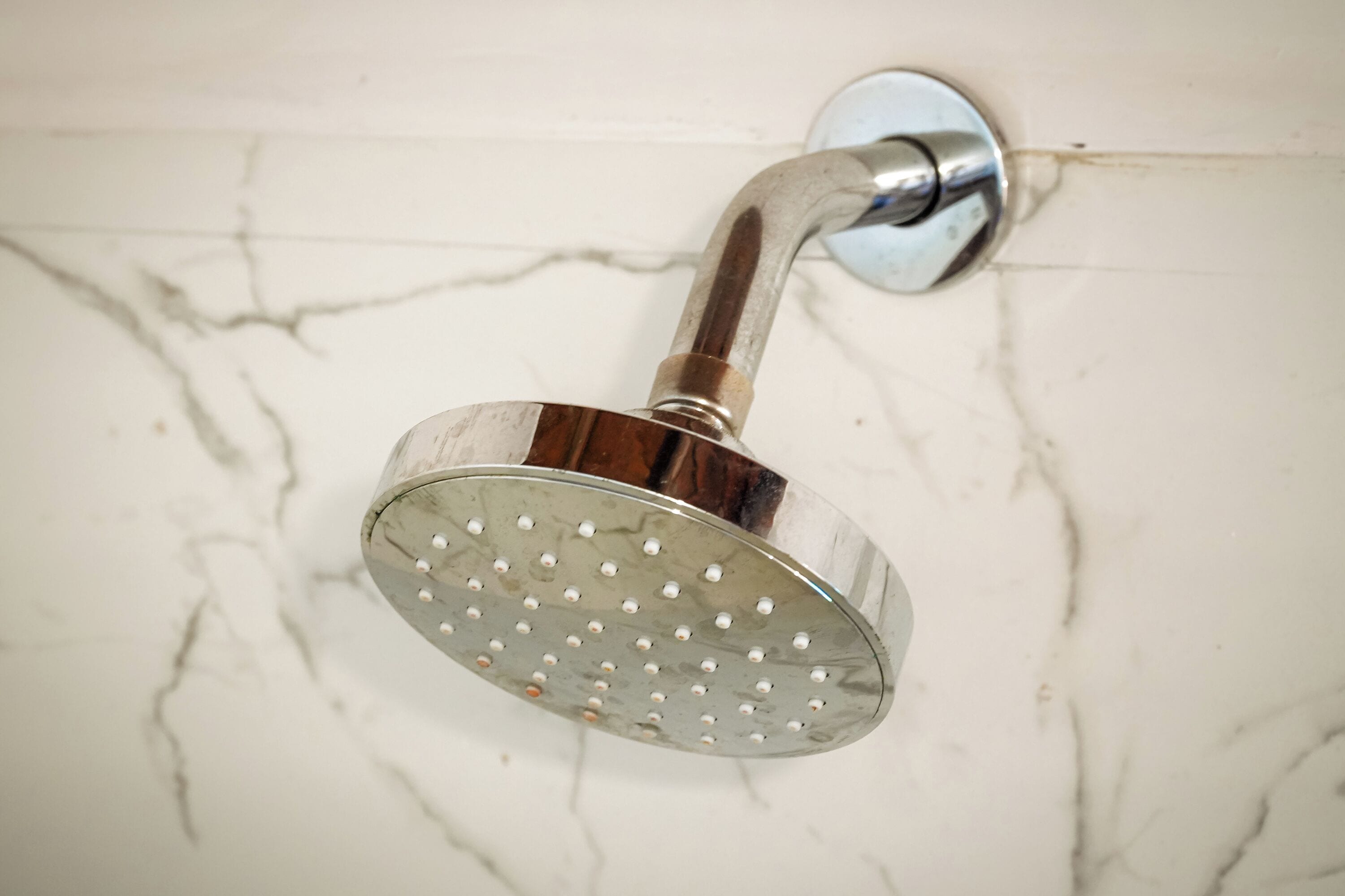 A showerhead mounted on a white marble wall with visible cracks.