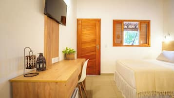 Quarto com escrivaninha de madeira, televisão fixada na parede, cama com colcha branca e janela com persianas.