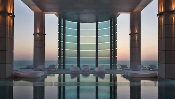 Una piscina infinita moderna con vistas despejadas al océano, rodeada de columnas y sillones de descanso.