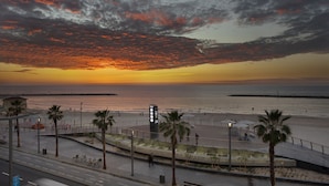 Vista de un atardecer costero con un paseo marítimo, palmeras y una ciclovía.