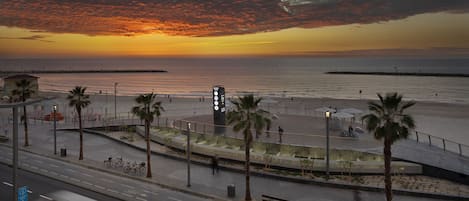 Vista de un atardecer costero con un paseo marítimo, palmeras y una ciclovía.