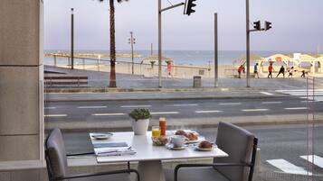 Ein Tisch mit Frühstücksangebot, ein Blumentopf und Blick auf Strand und Meer.