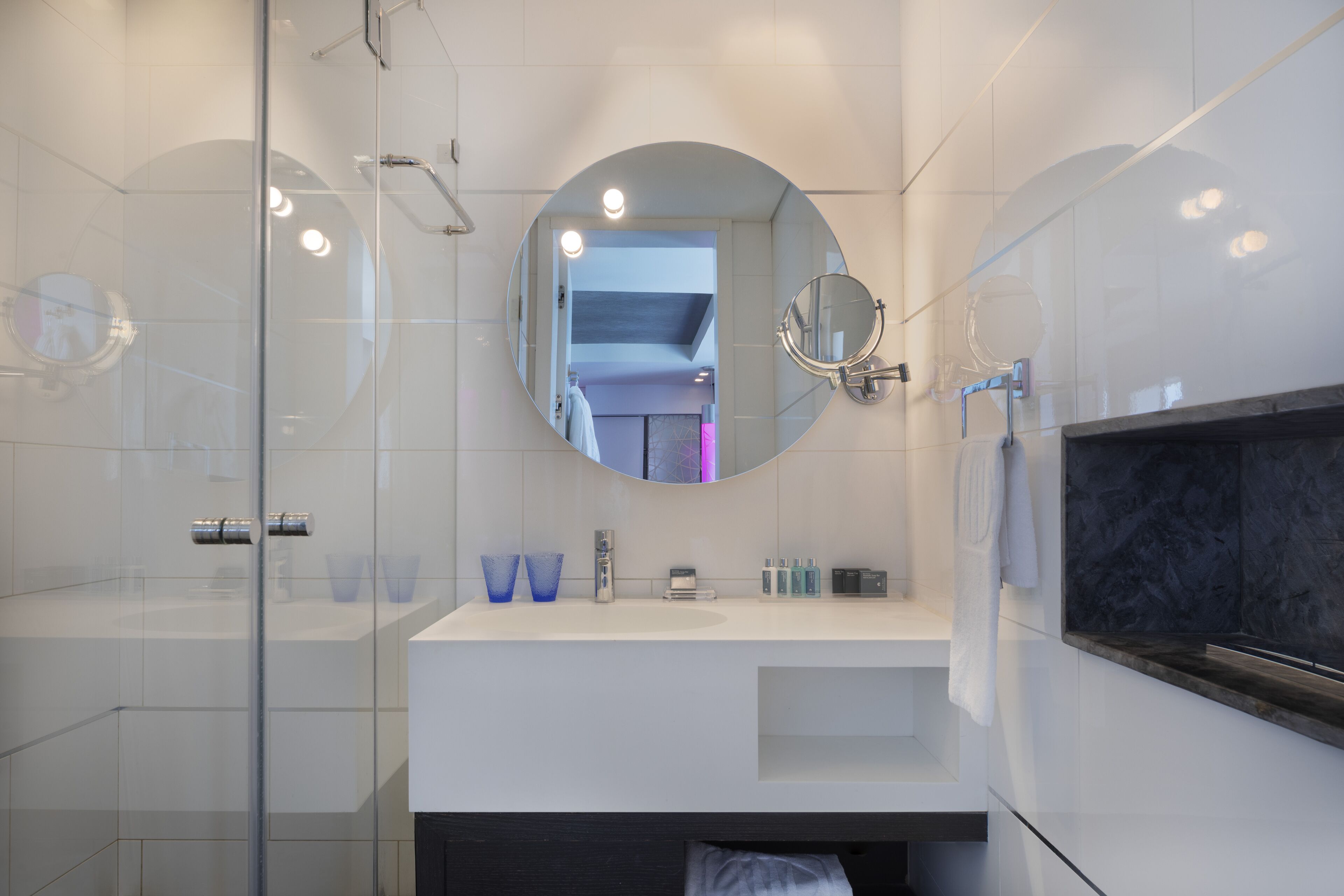 A modern bathroom with a glass shower enclosure, a white vanity with a mirror, and a marble accent wall.