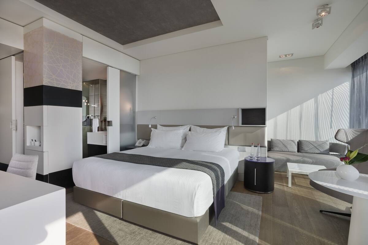 A modern hotel room with a large bed, a sofa, a desk, and a small table.