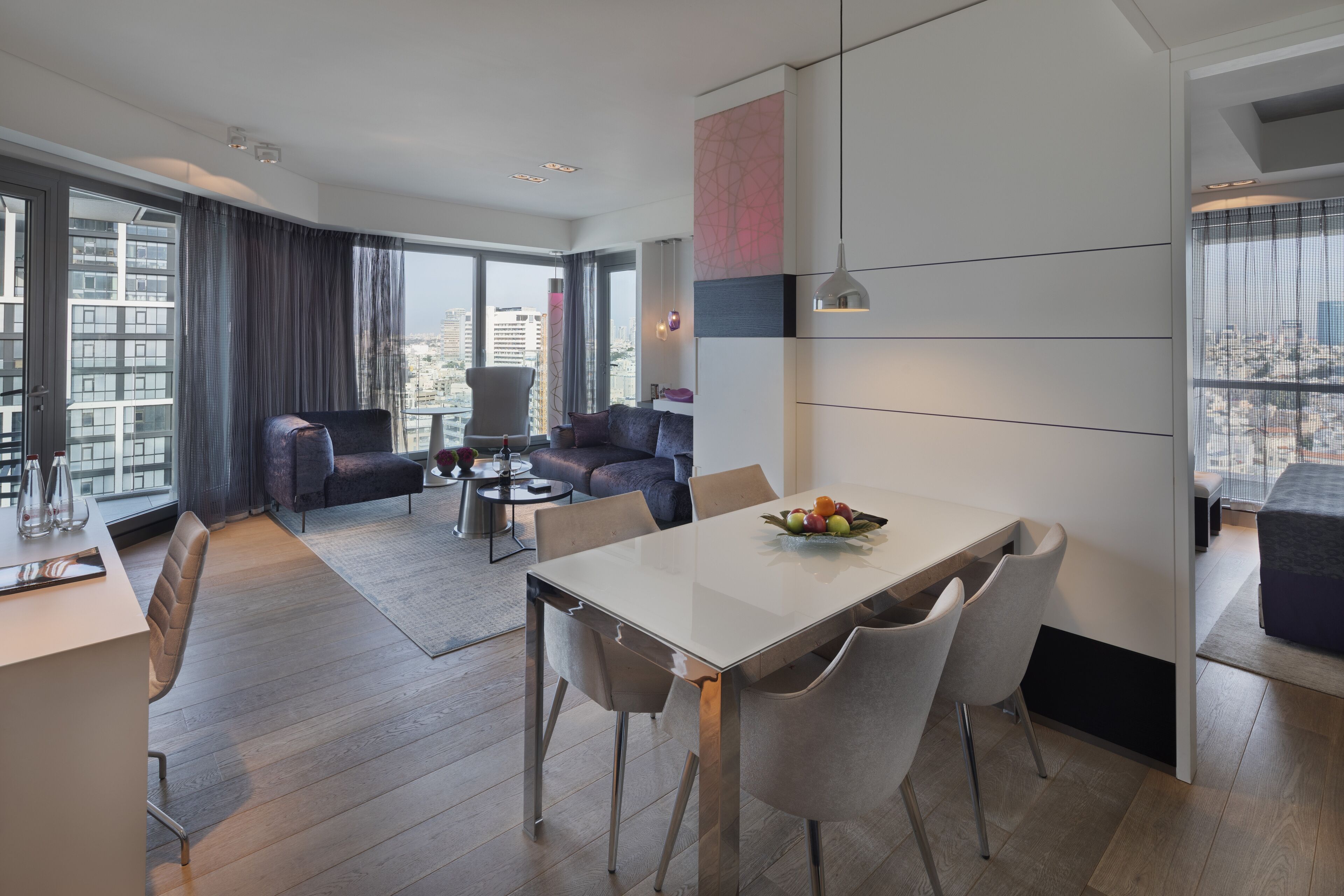A modern living room with a dining area, large windows, and a city view.
