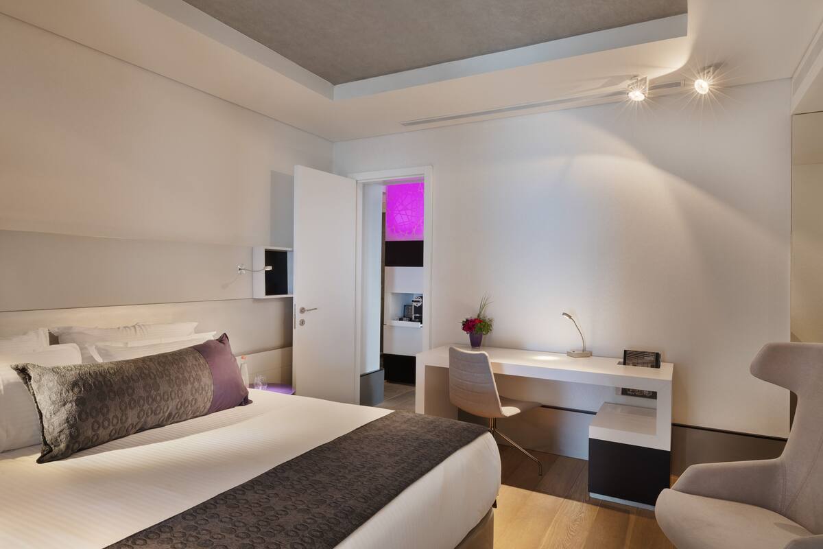 A modern hotel room with a large bed, a desk, and a chair.