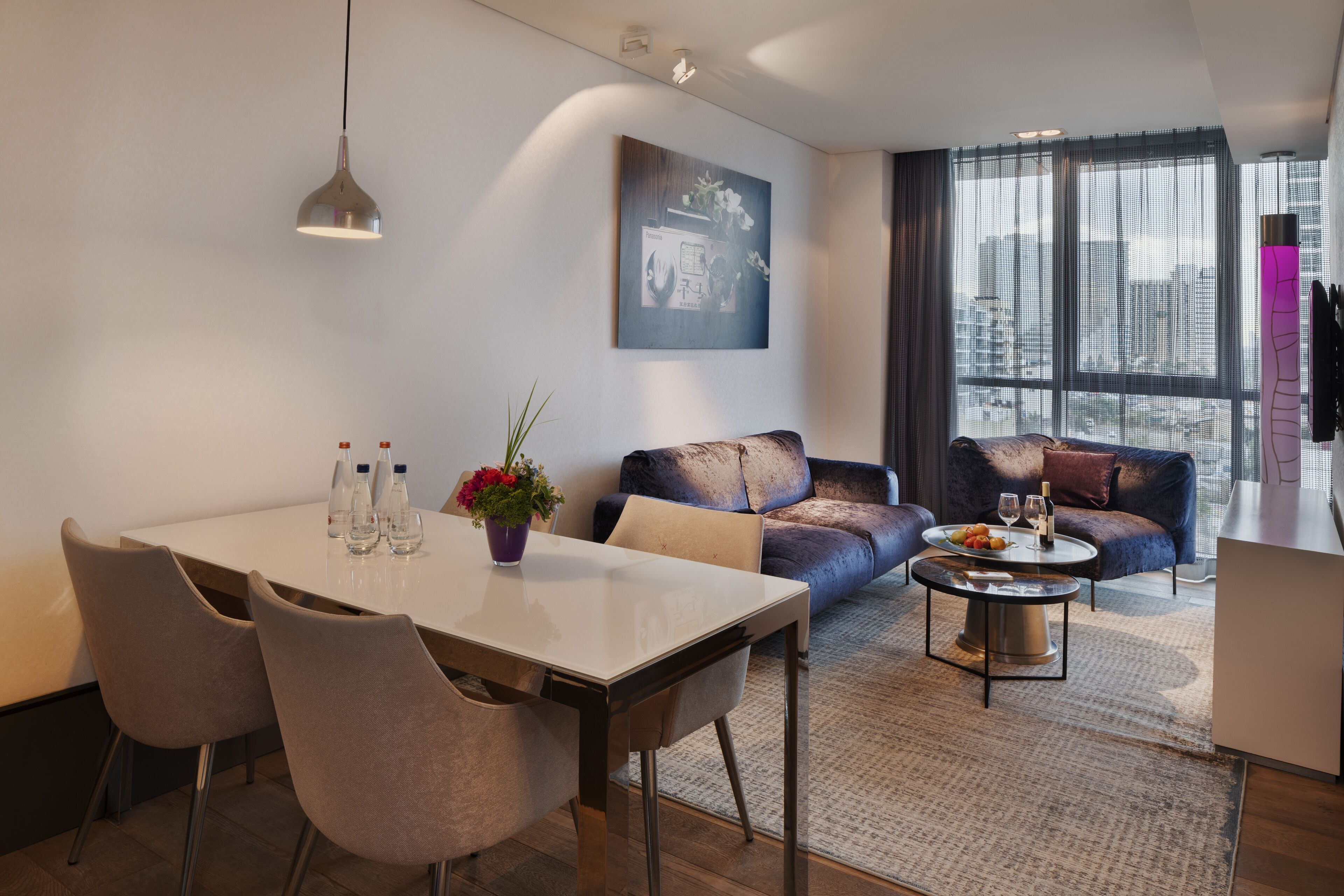 Ein modernes Wohnzimmer mit Essbereich, einer Couch, einem Couchtisch und einem großen Fenster mit Blick auf die Stadt.