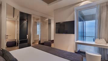 Una habitación de hotel moderna con una cama grande, un televisor montado en la pared y un balcón con vista al mar.