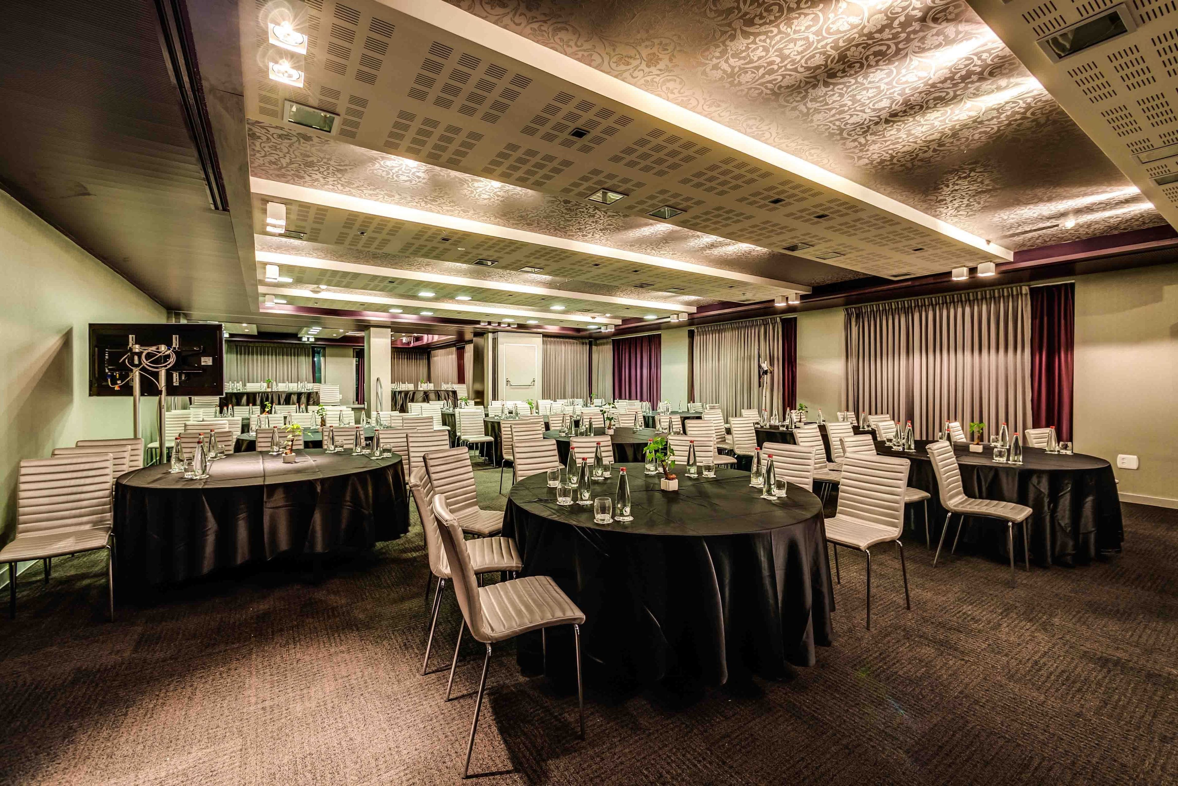 A conference room with multiple round tables, each surrounded by chairs, and equipped with water bottles and glasses.