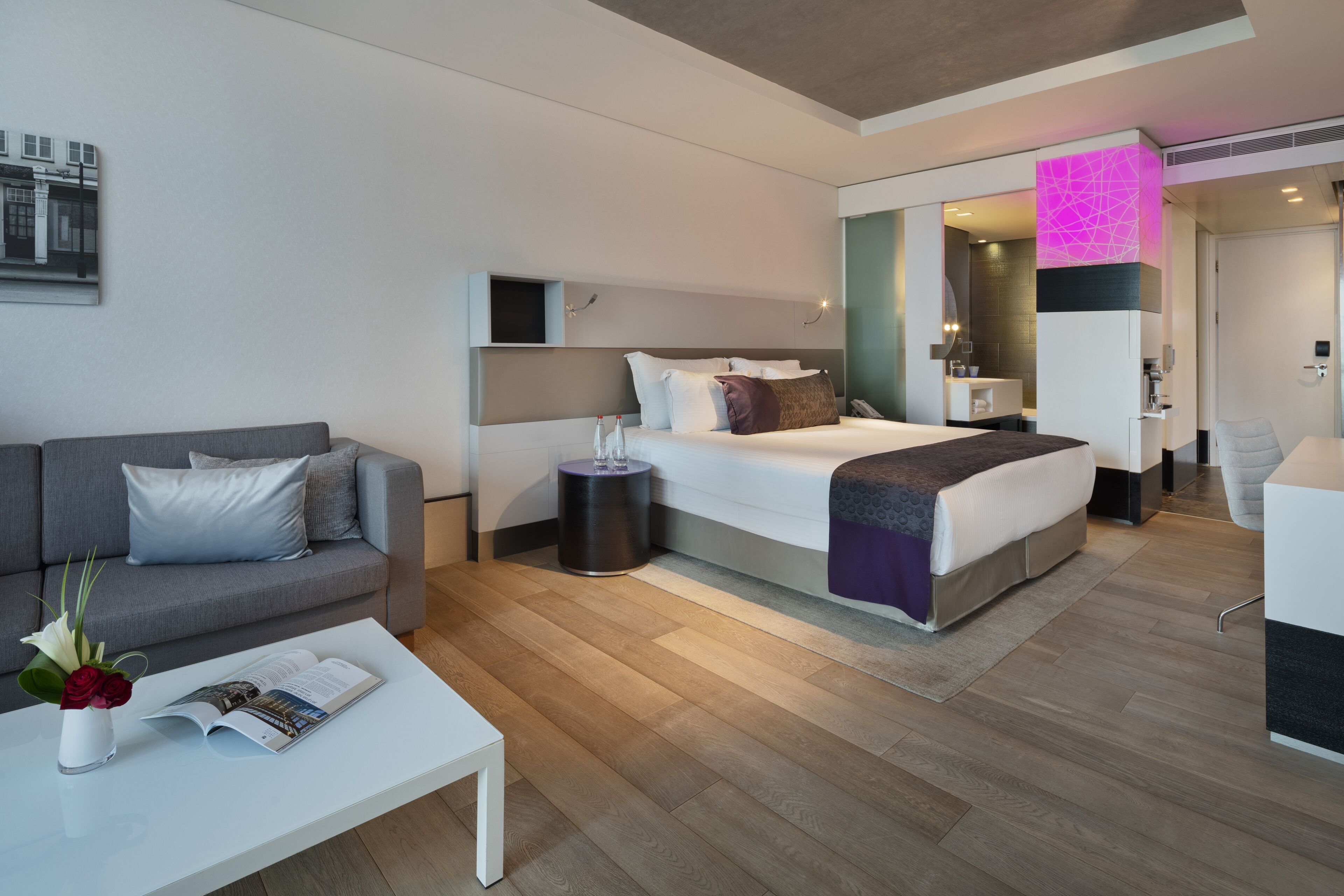 Una habitación de hotel moderna con una cama, un sofá, una mesita de café y una pequeña mesita auxiliar.