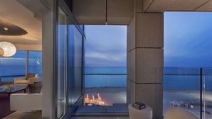 Una sala de estar moderna con un muro de vidrio con vistas a una playa al atardecer.