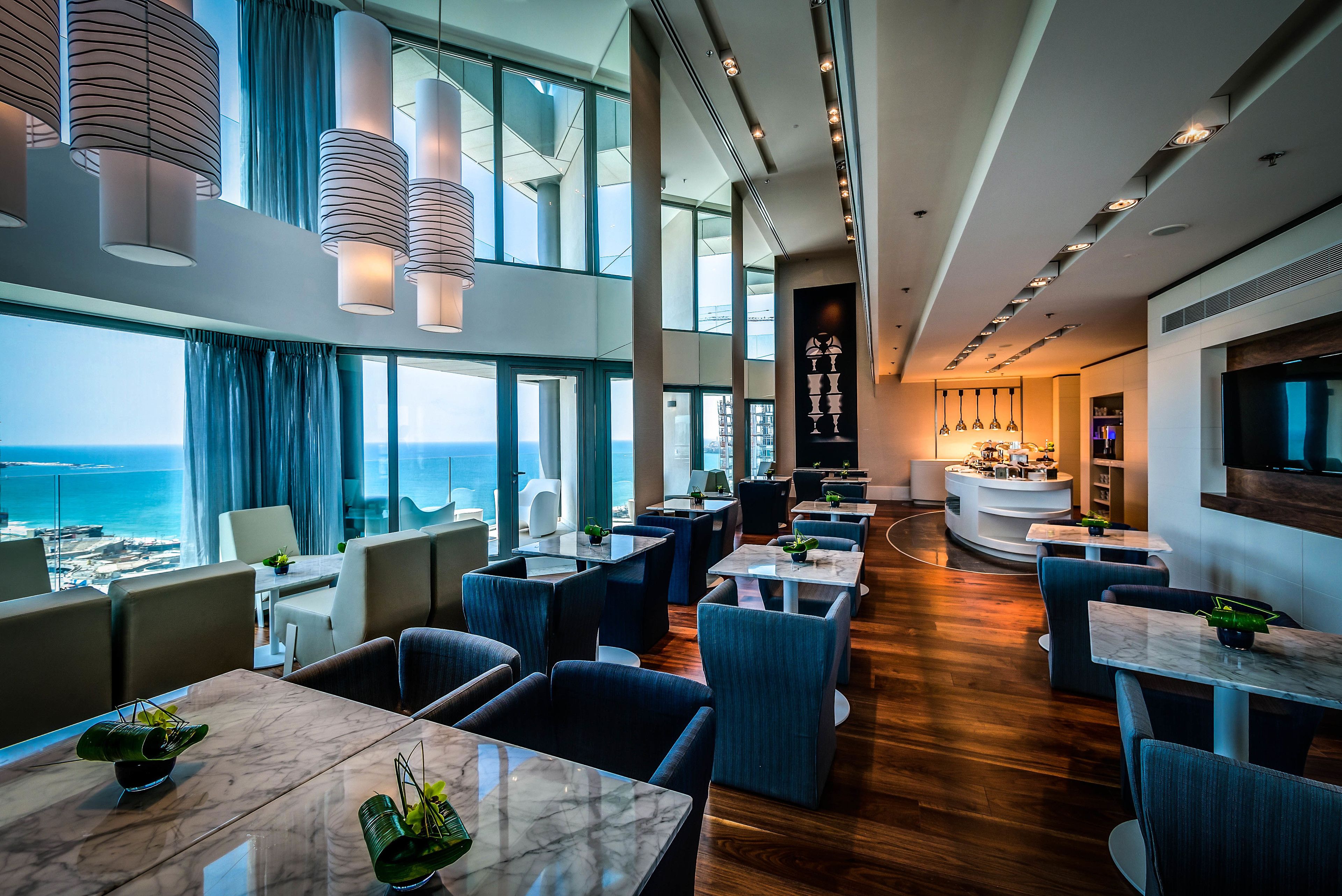 A modern hotel lobby with a view of the sea, seating areas, and a bar.