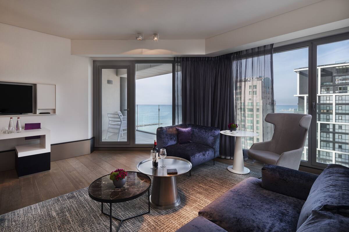 A modern hotel room with a balcony, a sofa, a coffee table, and a TV.