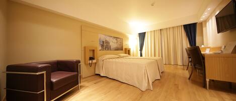 A hotel room with a bed, a desk, a chair, a sofa, and a TV on the wall.