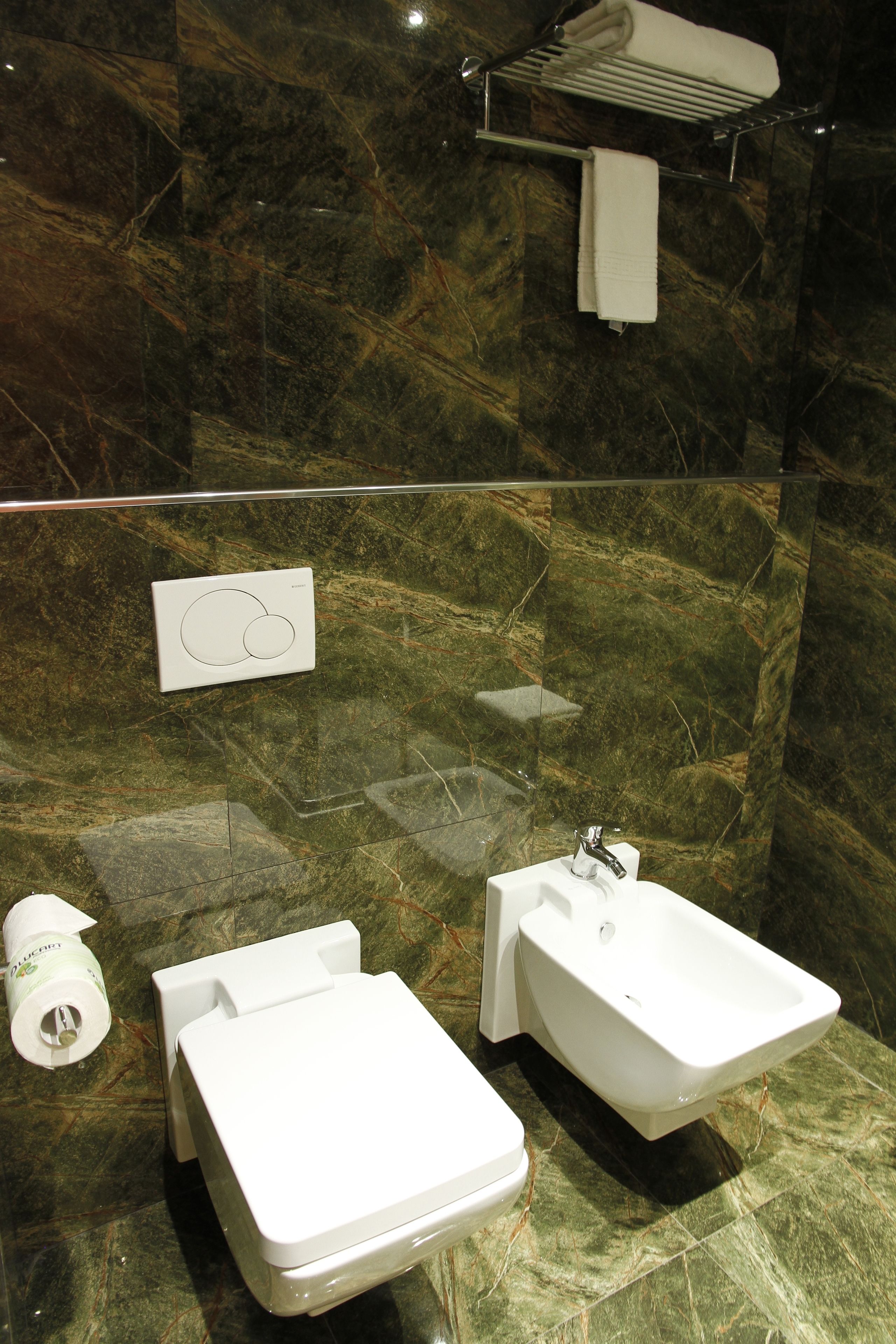 A bathroom with a marble wall, a white sink, a bidet, and a towel rack.