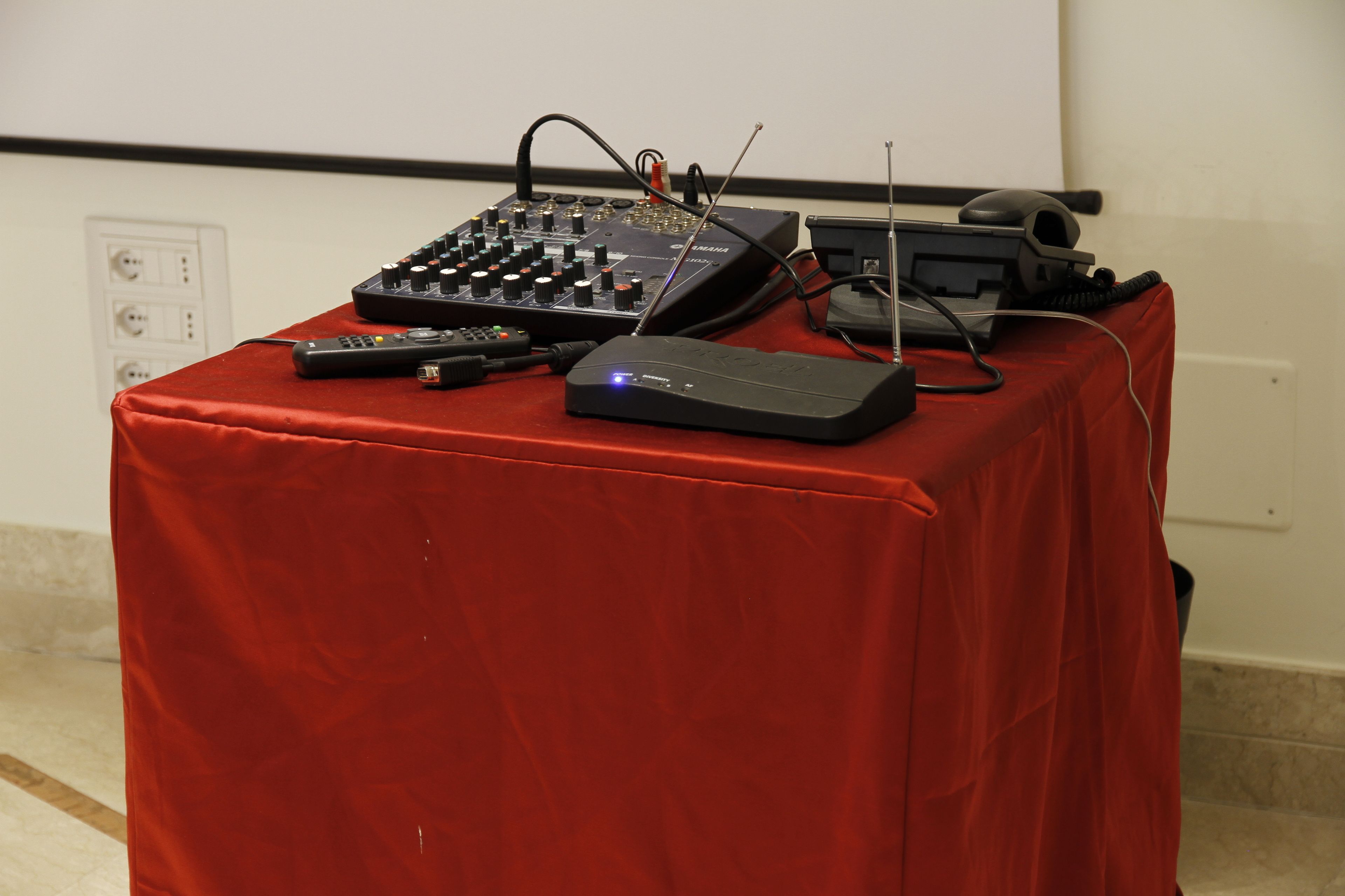 Un tavolo con apparecchiature elettroniche, un proiettore e un telecomando.