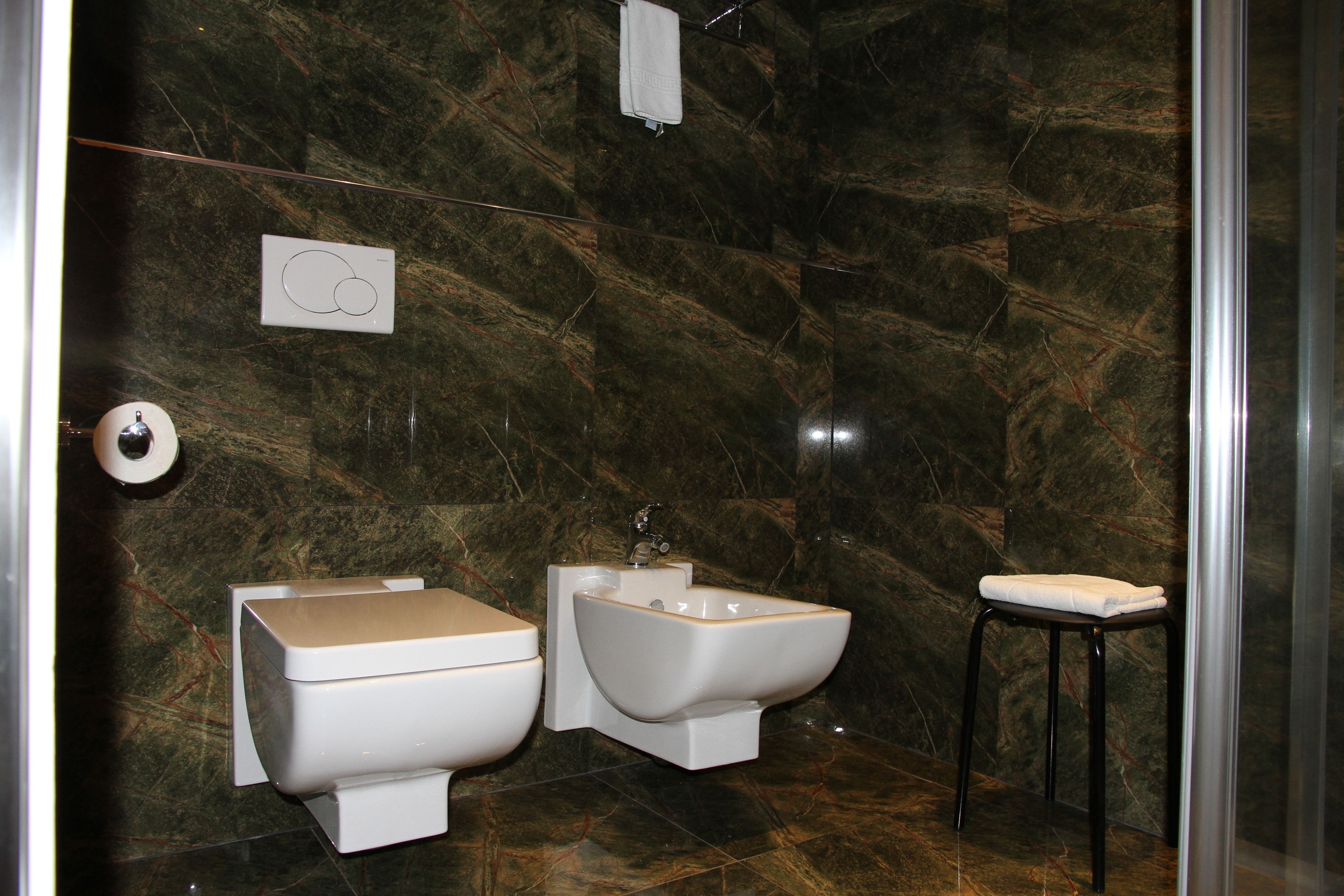 Un baño con inodoro, bidé y un taburete pequeño.