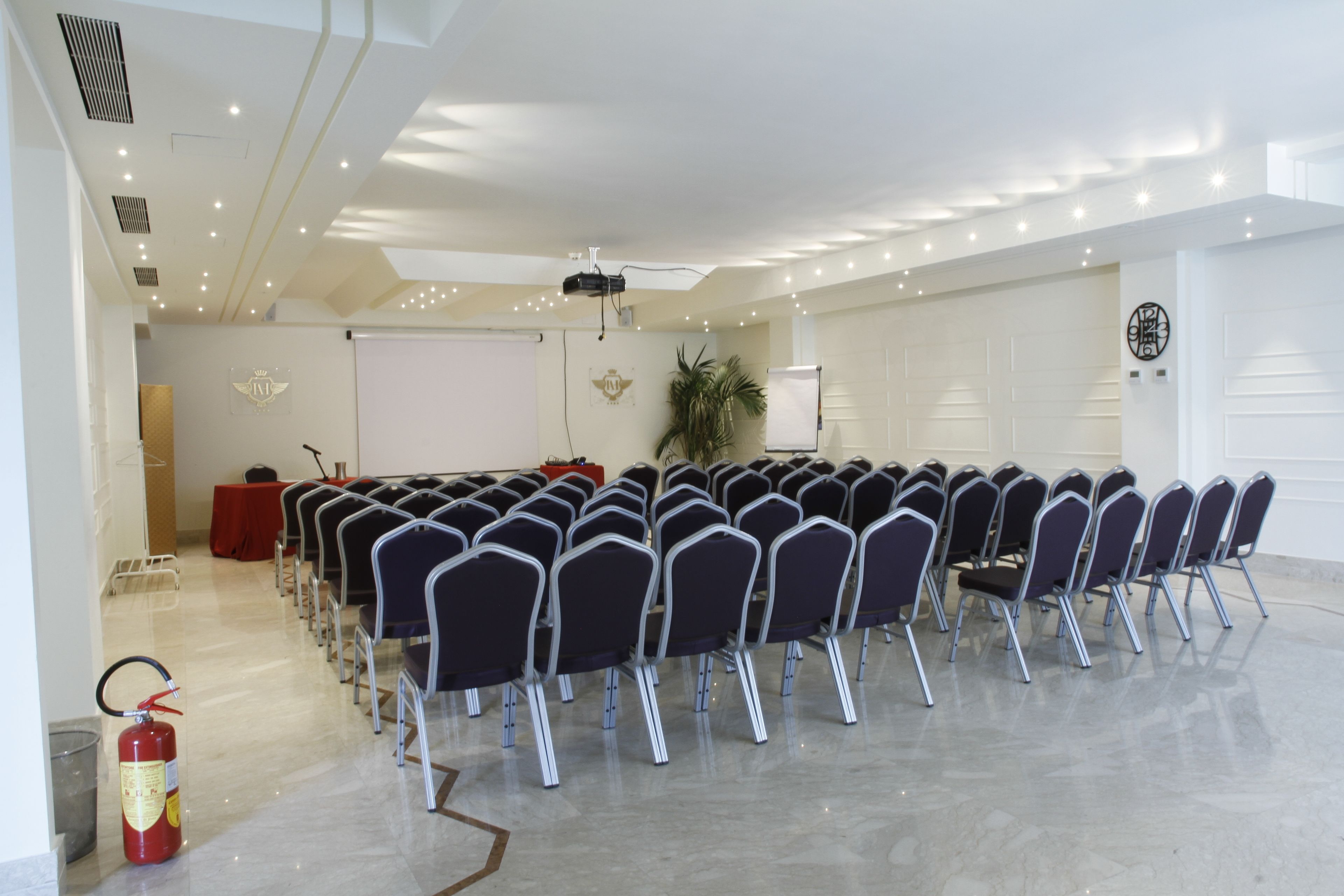 A conference room with rows of chairs, a whiteboard, a projector, and a fire extinguisher.