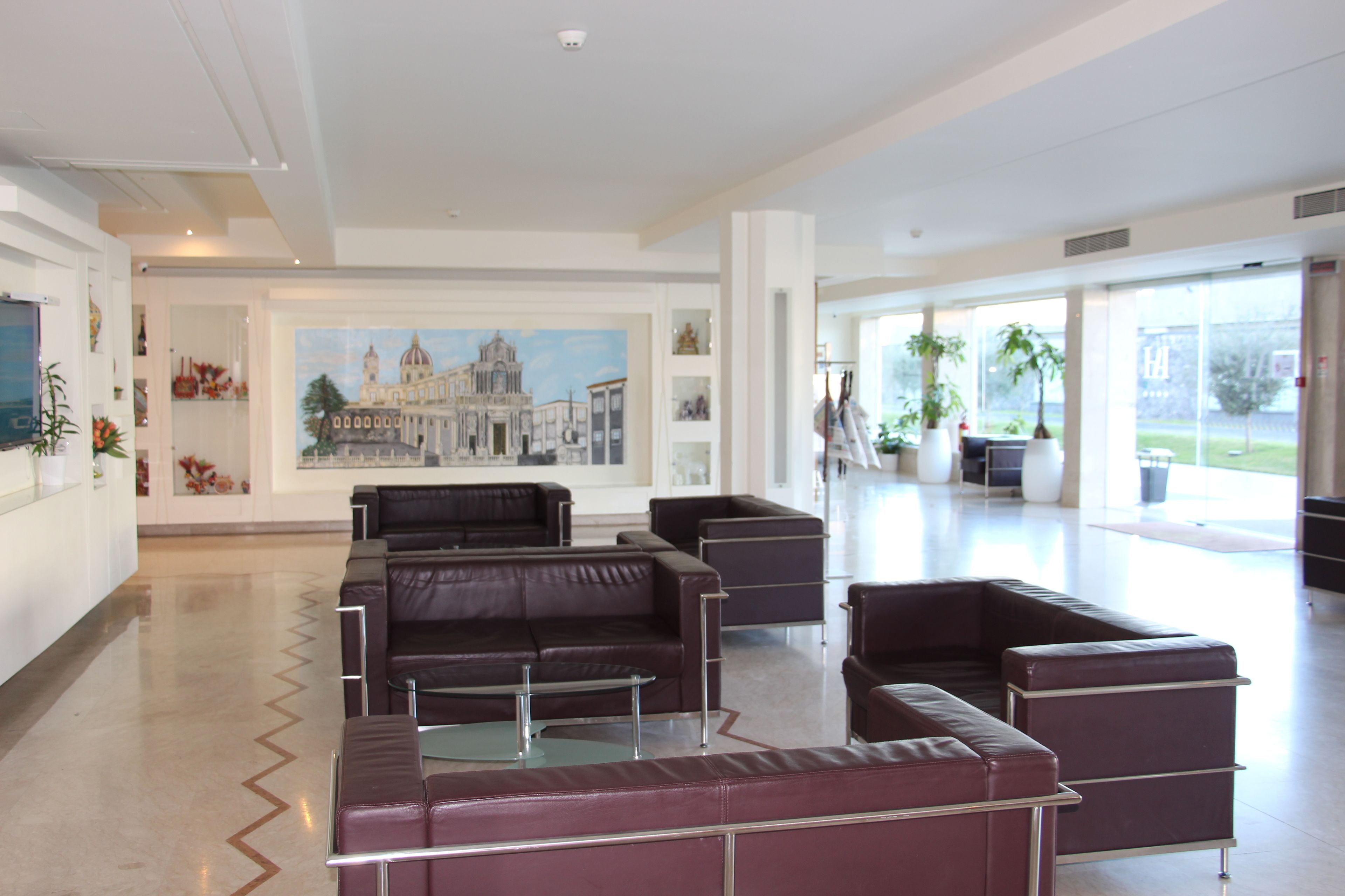 Un hall d’entrée spacieux, doté de canapés en cuir, d’une grande fresque murale et de larges fenêtres offrant une vue sur l’extérieur.