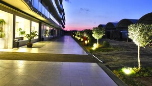 Un pasillo de hotel con suelo de baldosas, plantas en macetas y vista del cielo al anochecer.