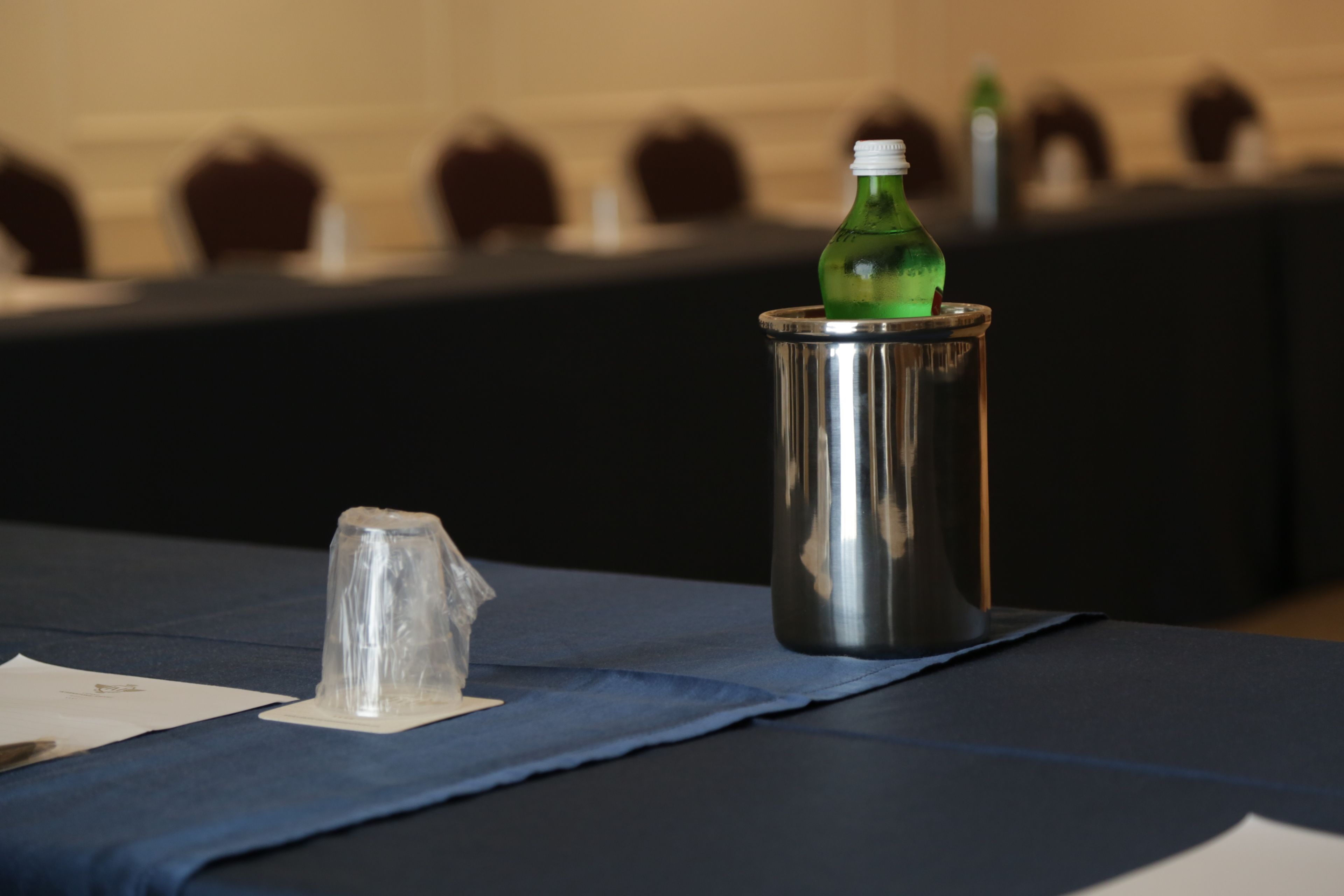A table with a clear plastic cup and a metal tumbler with a green bottle.