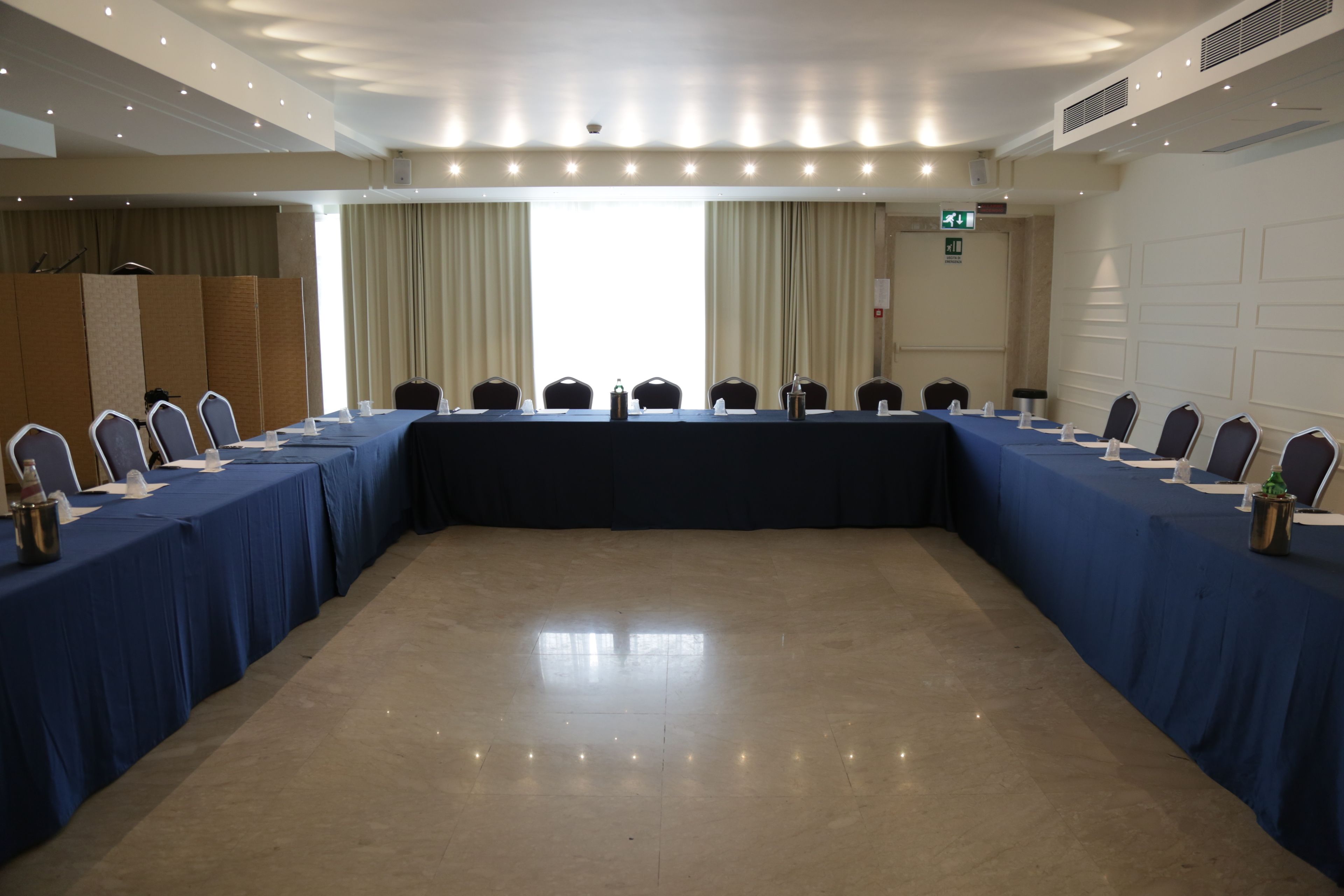 Ein Konferenzraum mit einem langen Tisch, Stühlen und einem Rednerpult.