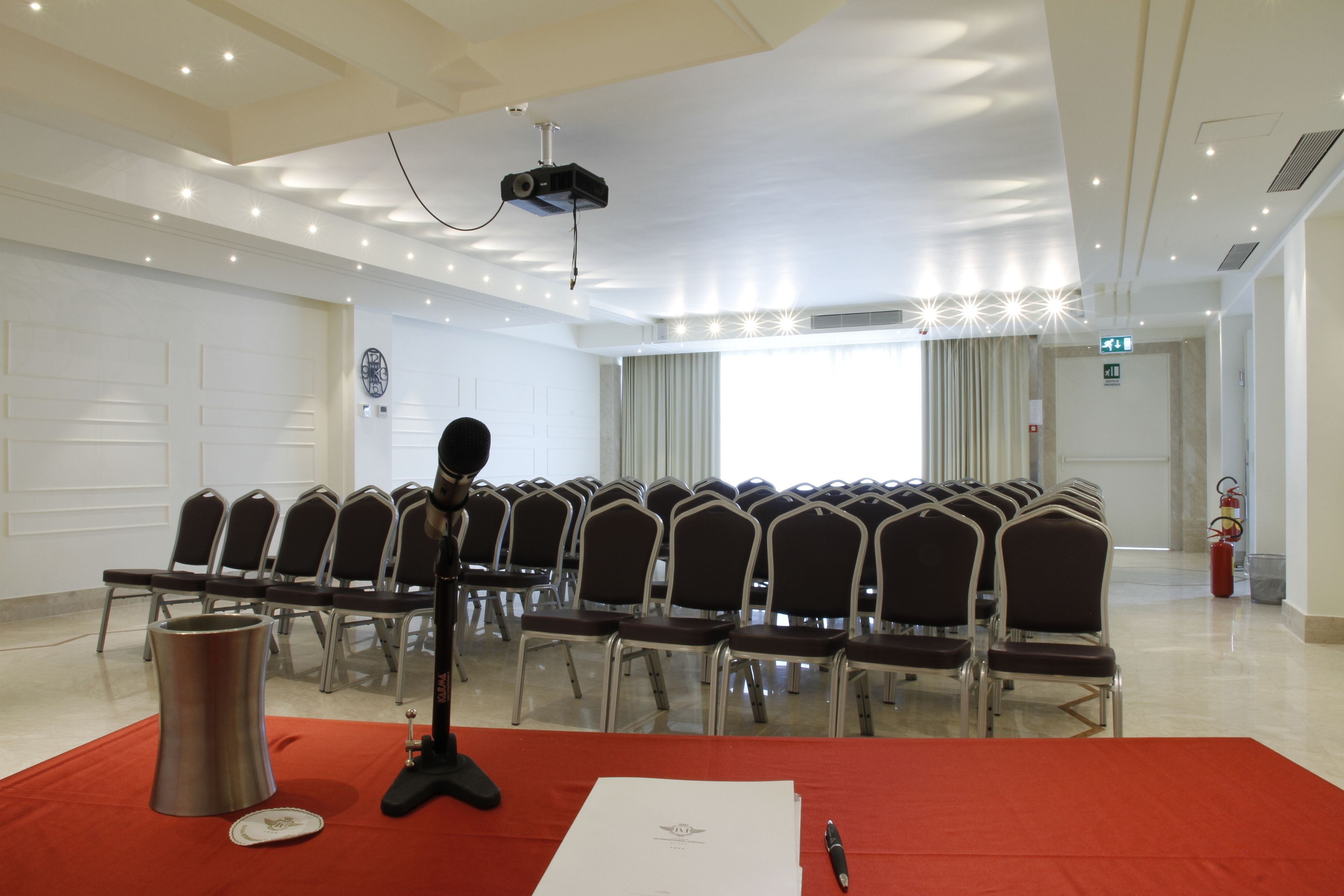 Una sala conferenze con file di sedie, un leggio, un proiettore e un estintore.