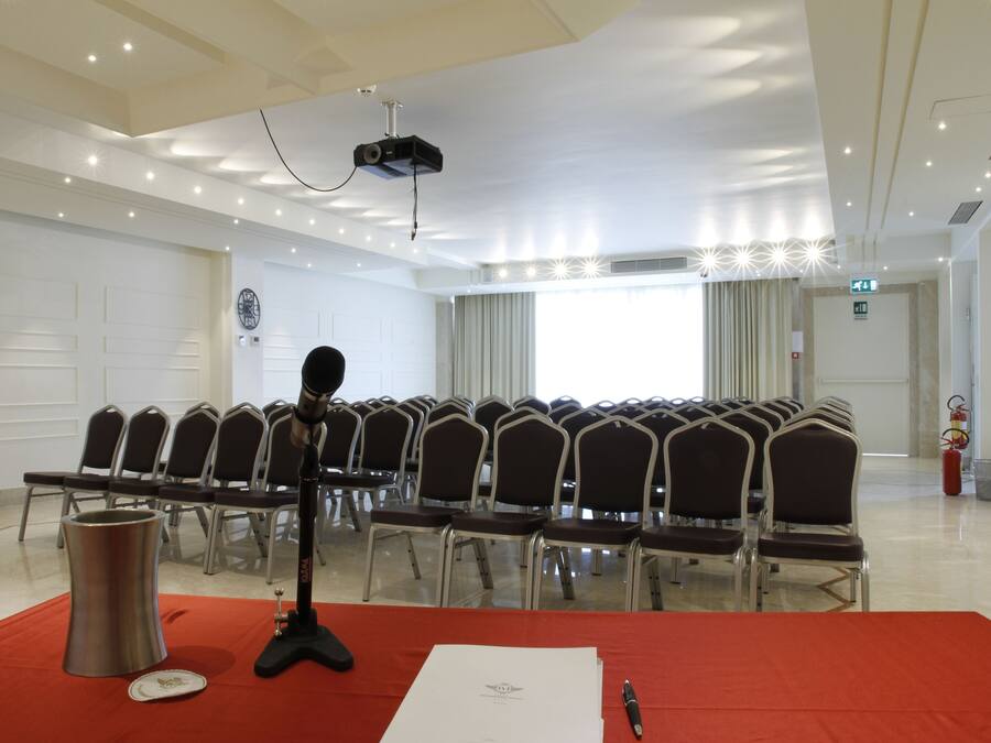 Una sala conferenze con file di sedie, un leggio, un proiettore e un estintore.