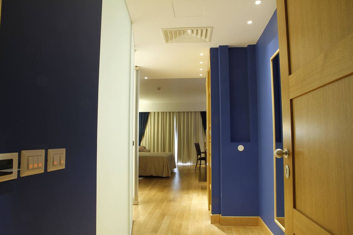 Un pasillo de hotel con una puerta de madera, una cama con cortinas y una silla.