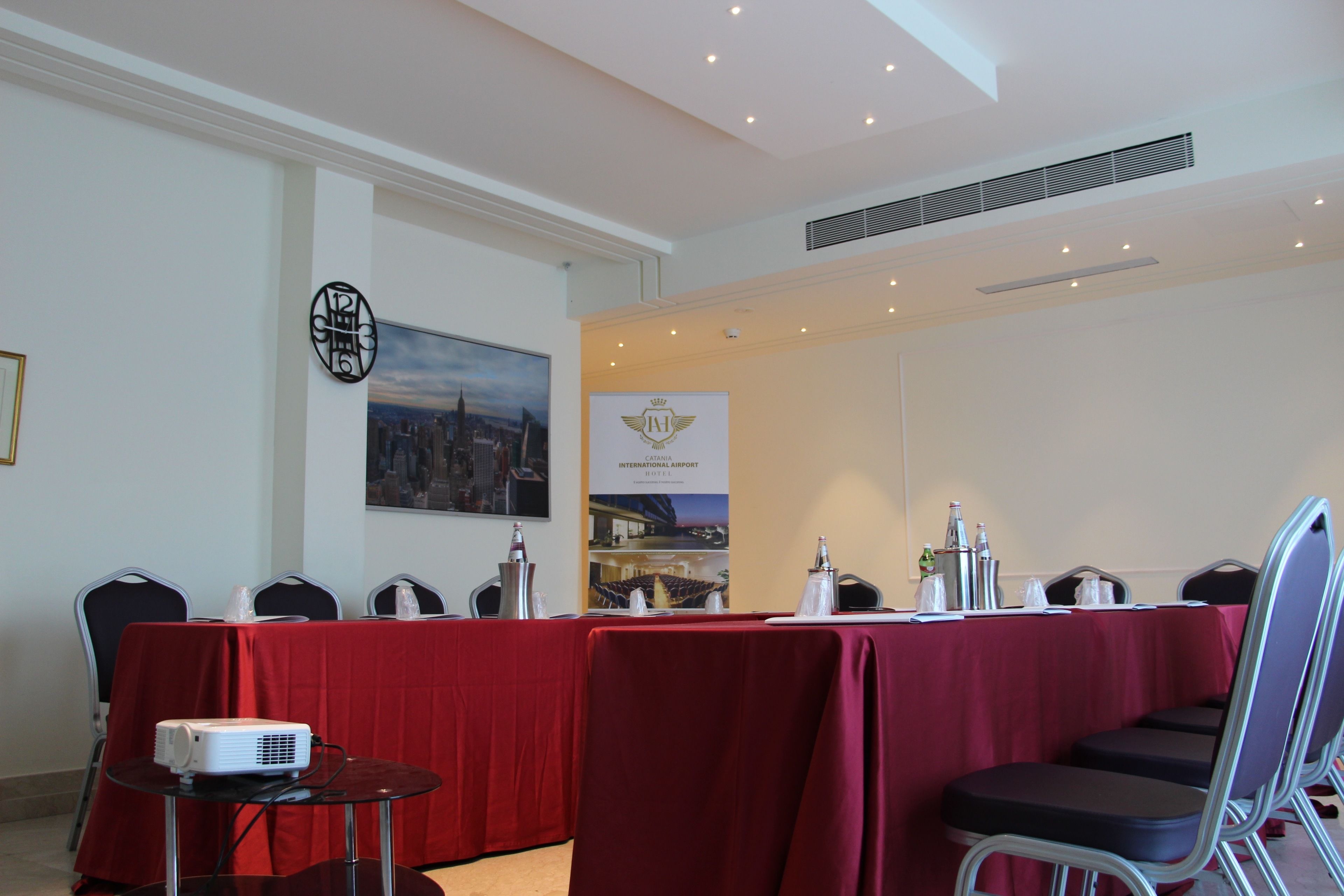 A conference room with a red table, chairs, a projector, and a banner on the wall.