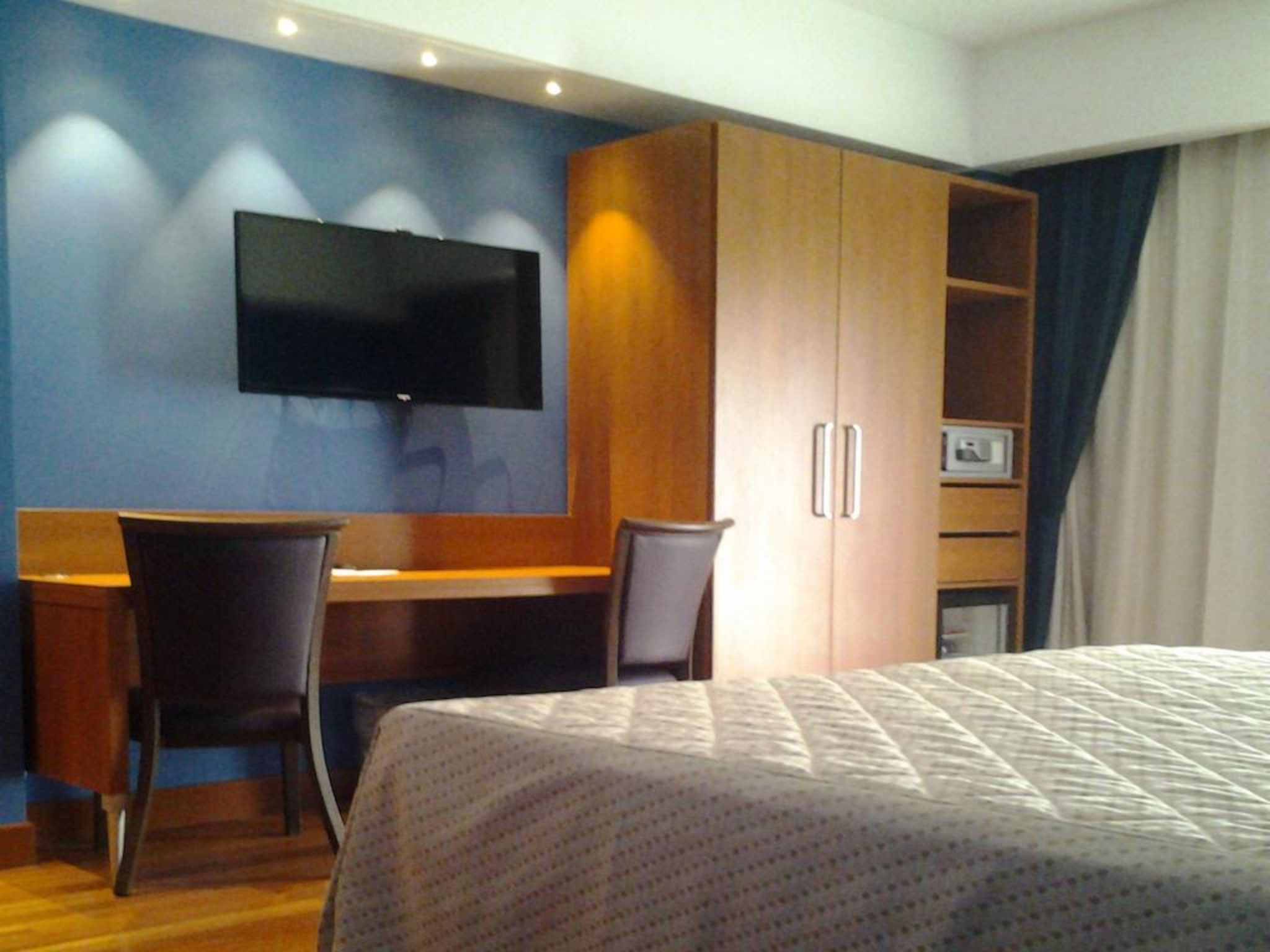 Habitació d'hotel amb un llit, escriptori amb cadira, televisió penjada a la paret i un armari.