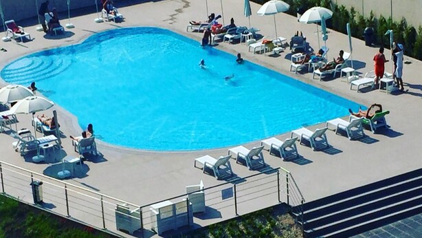 Piscina con sillones de playa y sombrillas, rodeada por una valla baja.