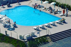 A swimming pool with lounge chairs and umbrellas, surrounded by a low fence. - Catania International Airport Hotel (Catania)