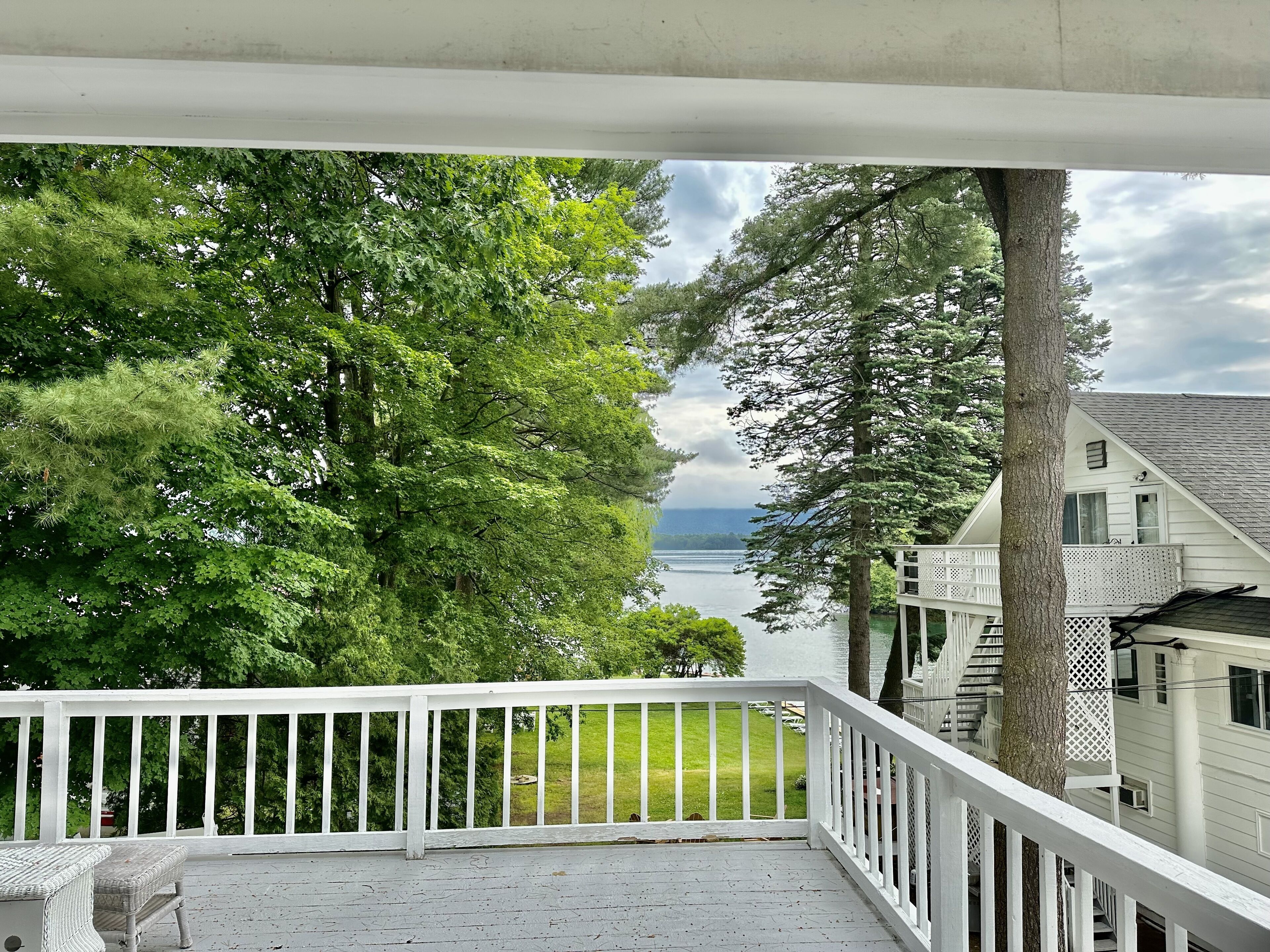 Une terrasse en bois avec une balustrade blanche donnant sur un lac, entourée d’arbres verdoyants.