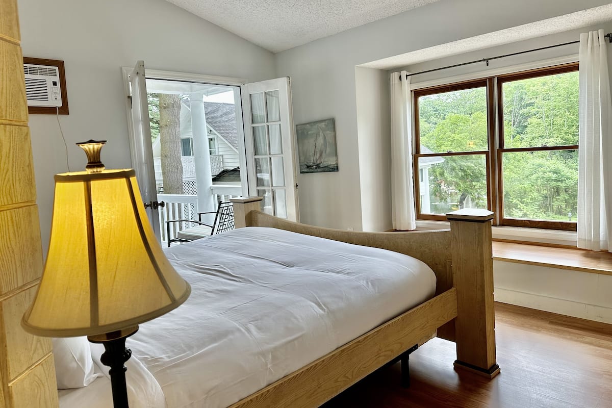 A bedroom with a bed, a lamp, a window with curtains, a chair, and a painting on the wall.