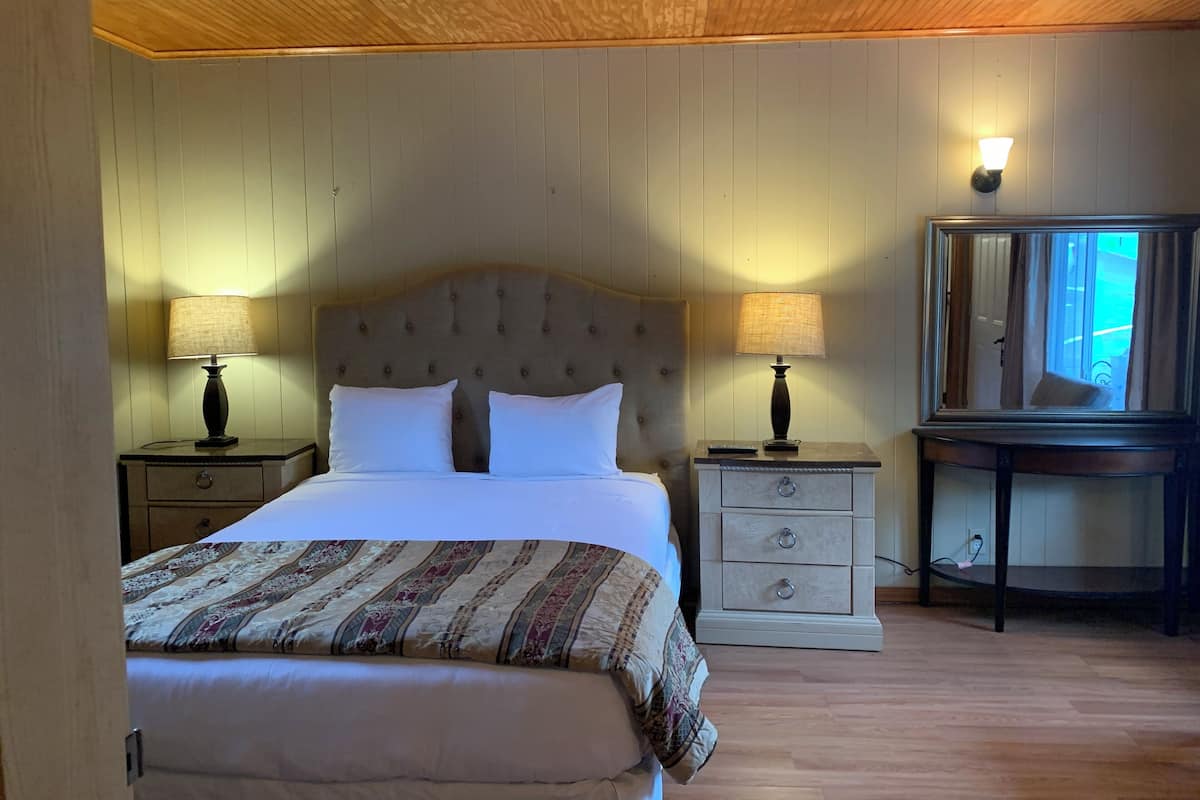A bedroom with a large bed, two bedside tables with lamps, a dresser, and a mirror.