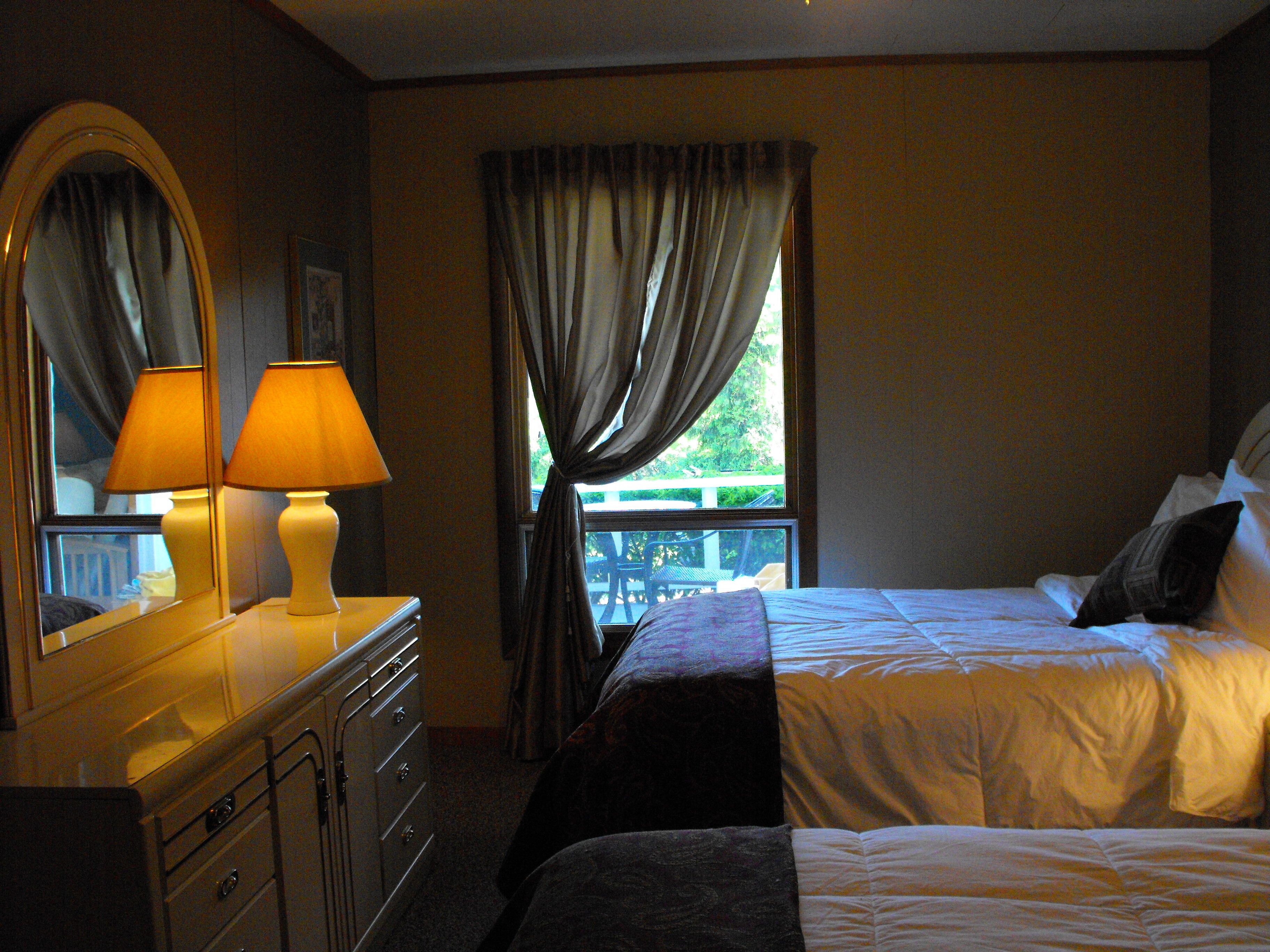Habitación de hotel con cama, cómoda, espejo y ventana con cortinas.